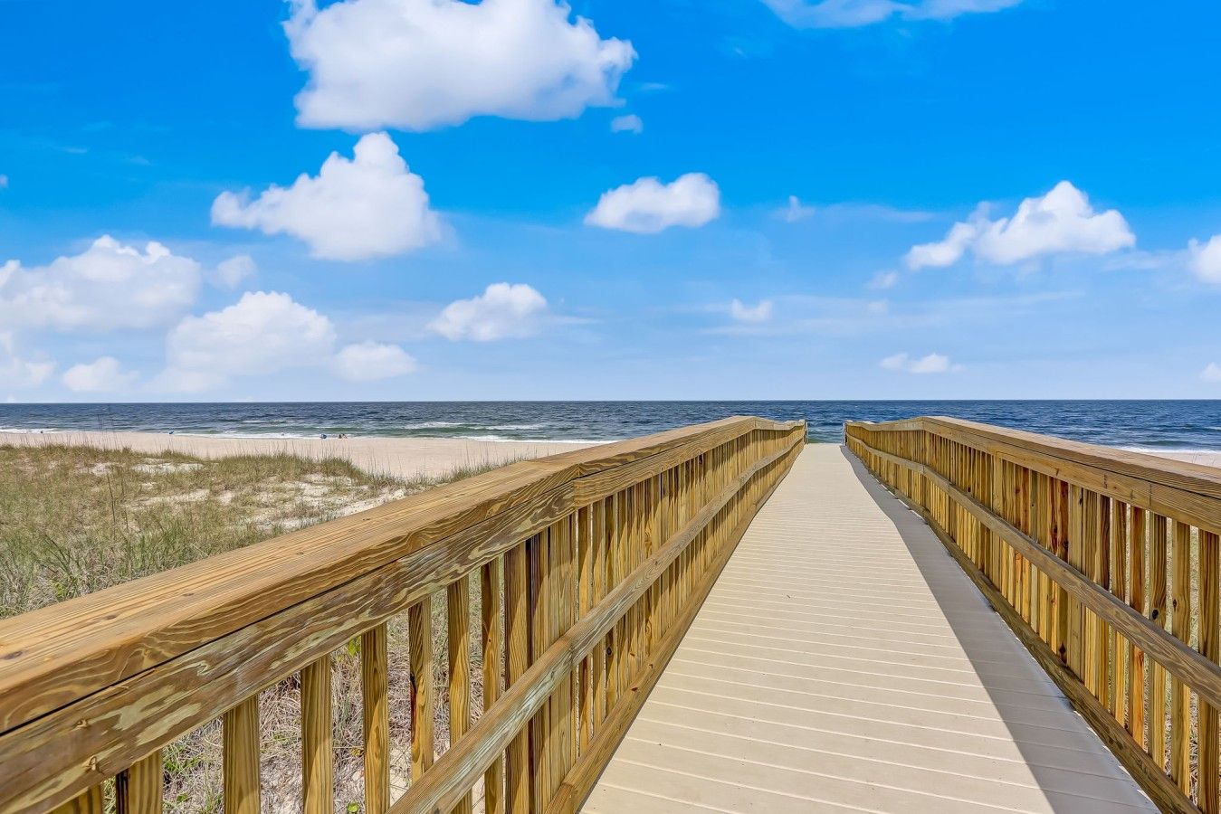 Une promenade en bois menant à une plage, avec un ciel dégagé.