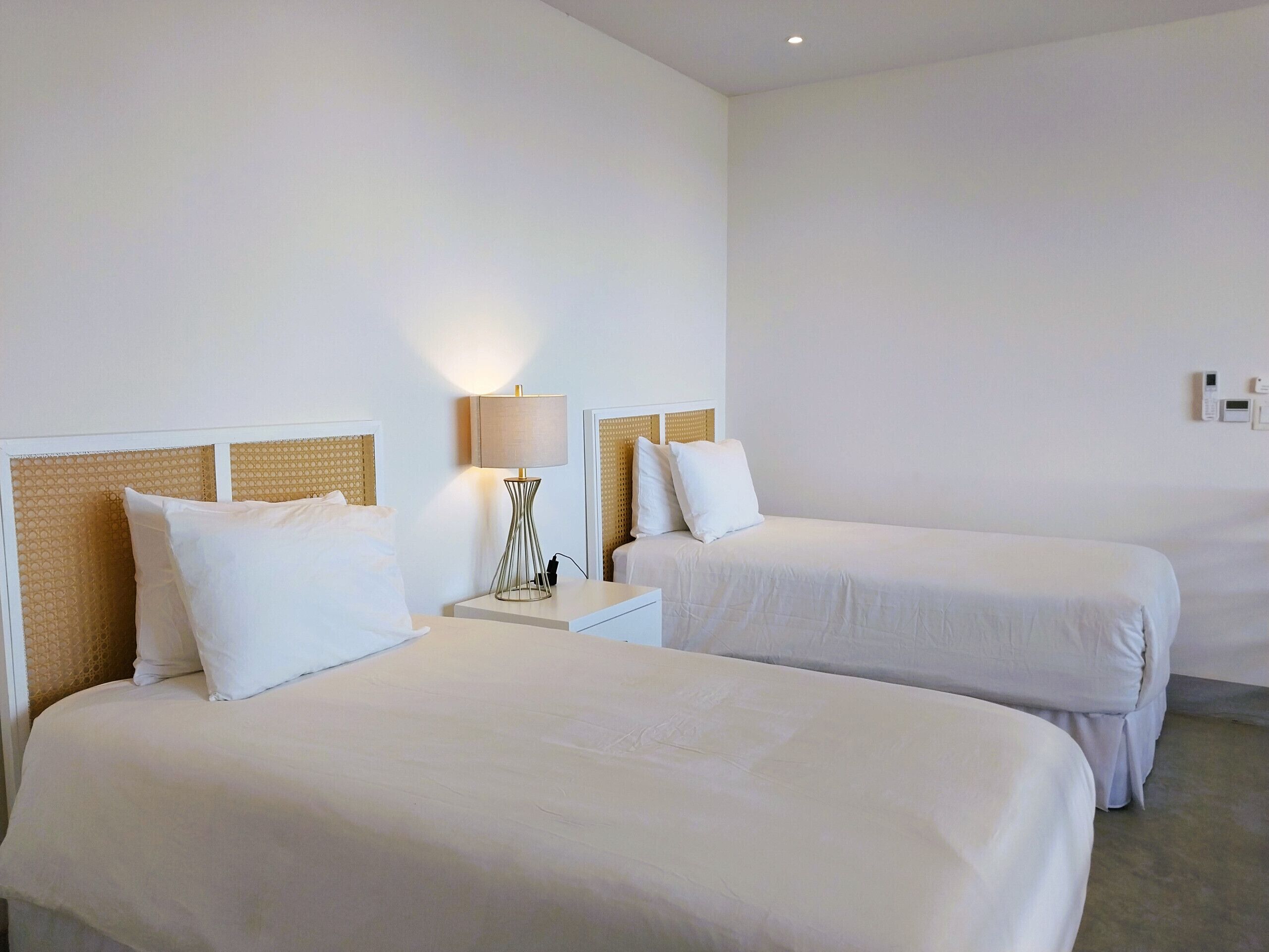 Une chambre d’hôtel avec deux lits simples, une table de chevet avec une lampe et un thermostat fixé au mur.