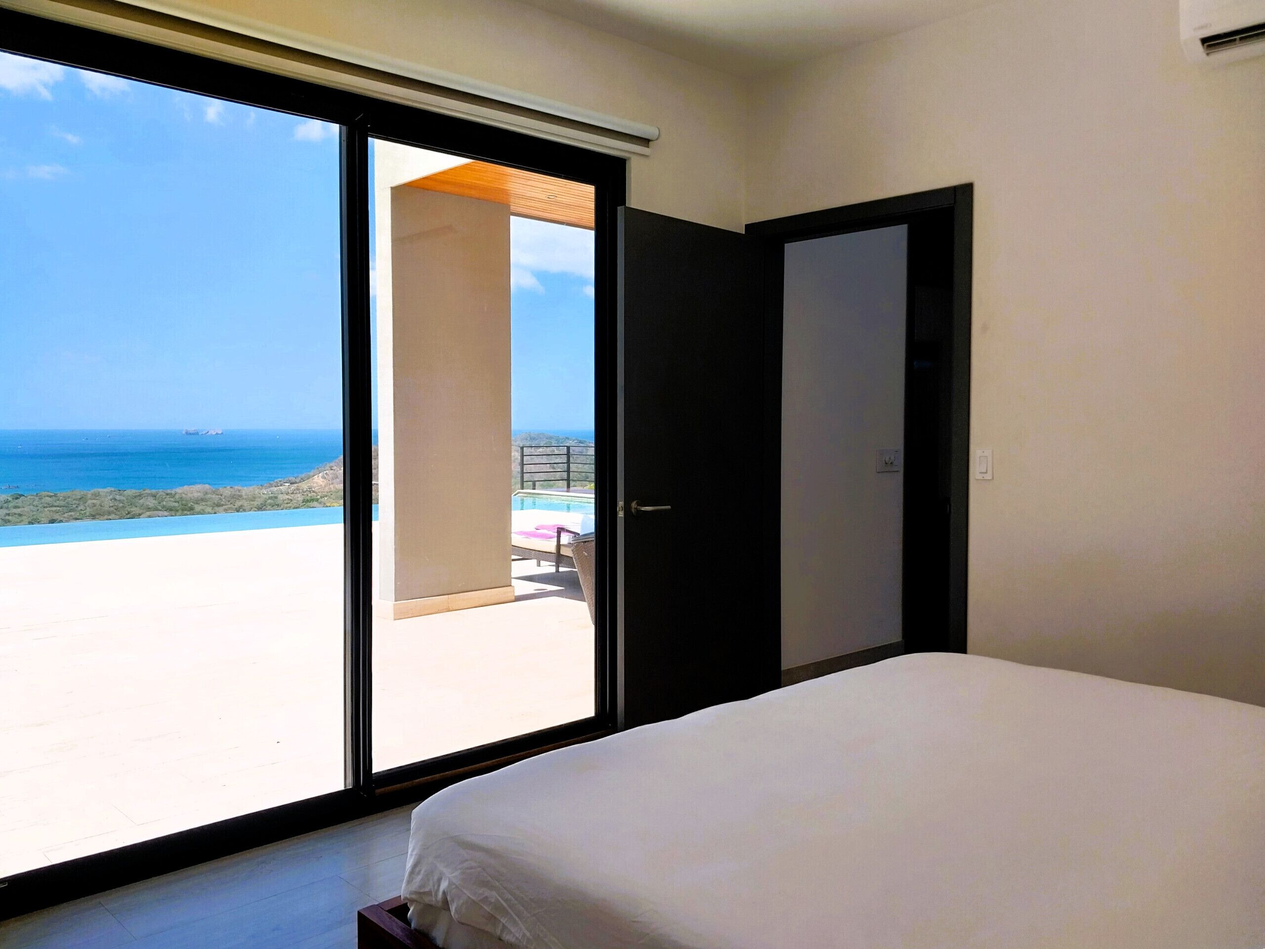 Un dormitorio con un amplio ventanal corredera que da a un balcón con vistas al mar.