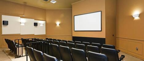 A conference room with rows of black chairs, a large projection screen, and a whiteboard.