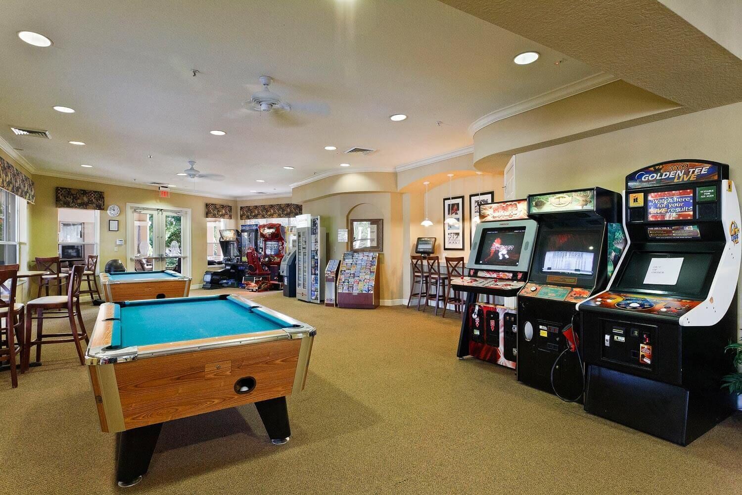 A pool table, arcade games, and a billiards table in a room with carpeted floors and recessed lighting.