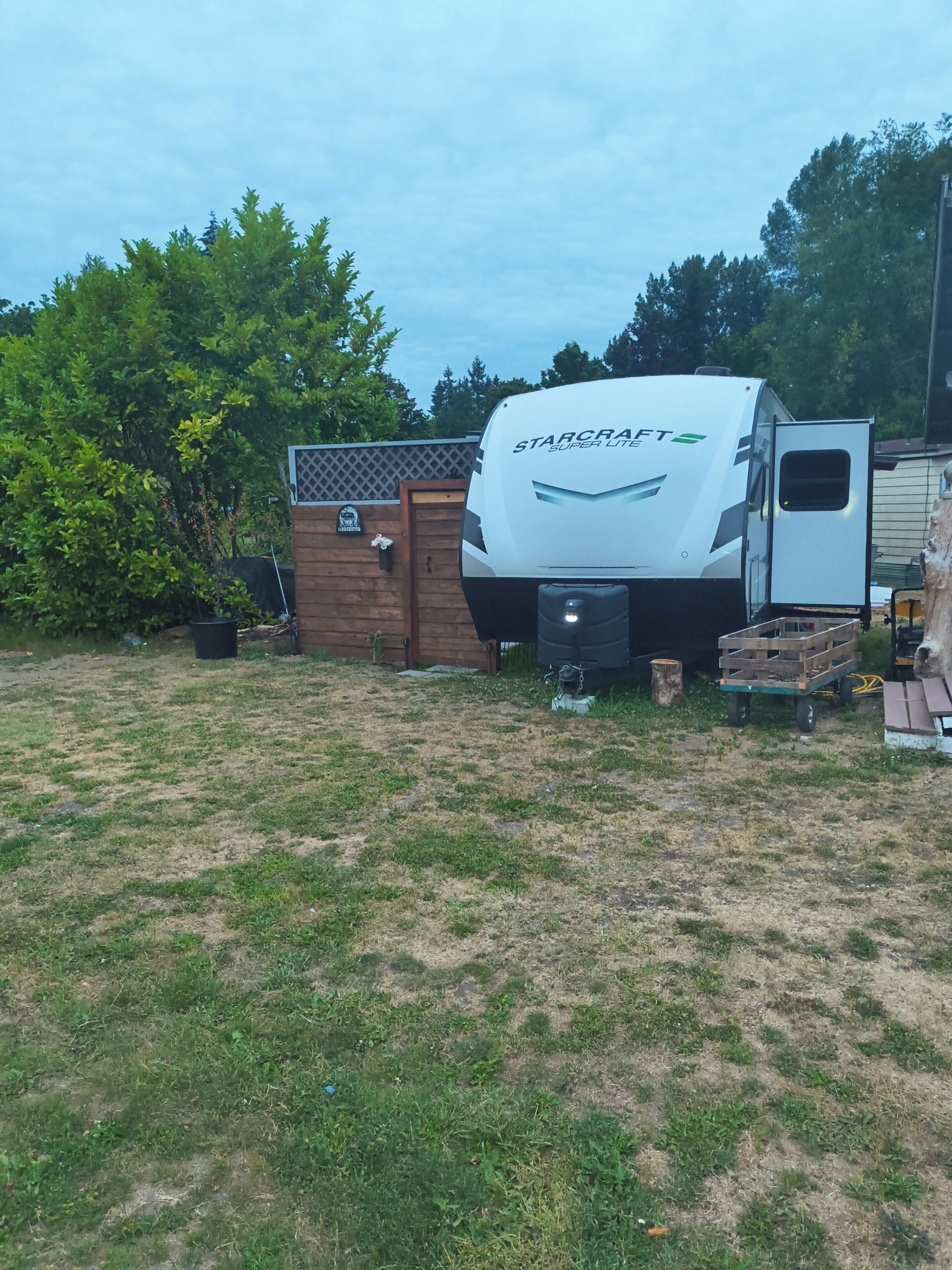 Una caravana StarCraft Super Lite estacionada en un área con césped, una cerca de madera y árboles al fondo.