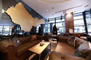 Un espacio de descanso acogedor con sofás de cuero y una mesa de madera, ventanas amplias con vista a la calle y un diseño de pared singular.