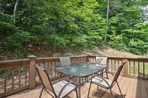 A wooden deck with a glass table and chairs, surrounded by dense forest. - Mountain Cabin Getaway w/Hot Tub & Fire Pit! (Townsend)