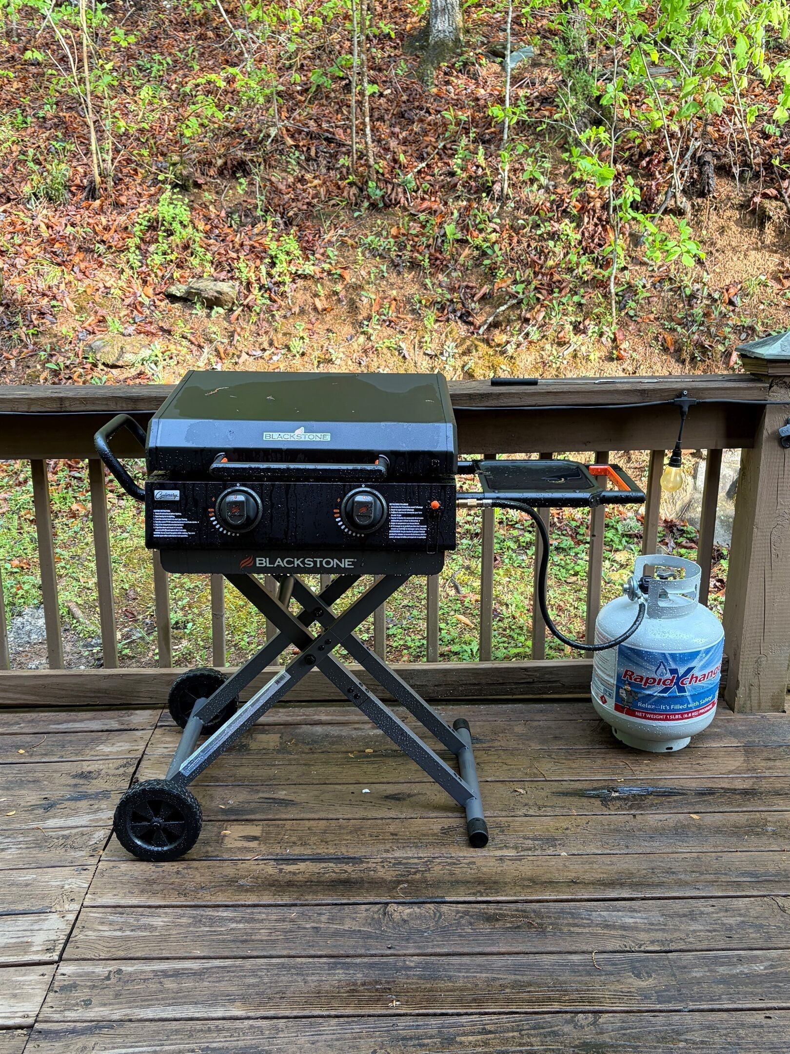 Una parrilla portátil sobre una terraza de madera, con un tanque de propano a su lado.