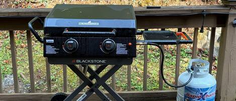 Una parrilla portátil sobre una terraza de madera, con un tanque de propano a su lado.