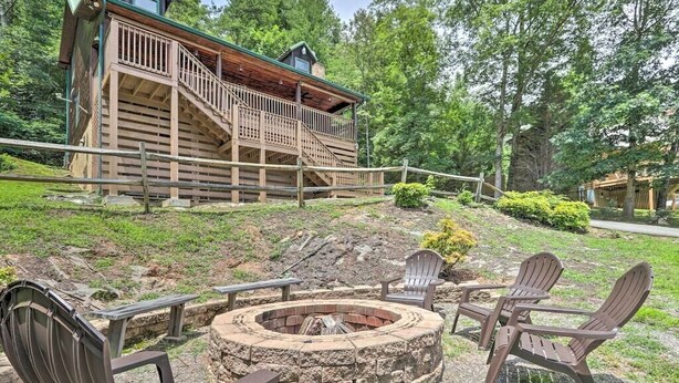 Eine Holzhütte mit einem Steinkamin und Adirondack-Stühlen, umgeben von einer Holzterrasse und einer Steinmauer.