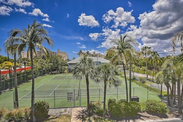 A tennis court surrounded by palm trees and buildings.