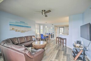 A spacious living room with a brown leather sofa, a round coffee table, and a dining area with blue chairs.