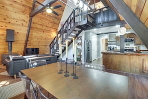 A spacious living area with a high ceiling, a wooden staircase, and a modern kitchen.