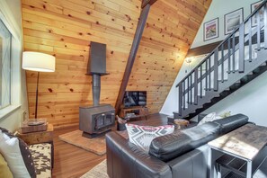 Ein gemütliches Wohnzimmer mit Holzboden, Kamin, Ledersofa und einer Treppe.