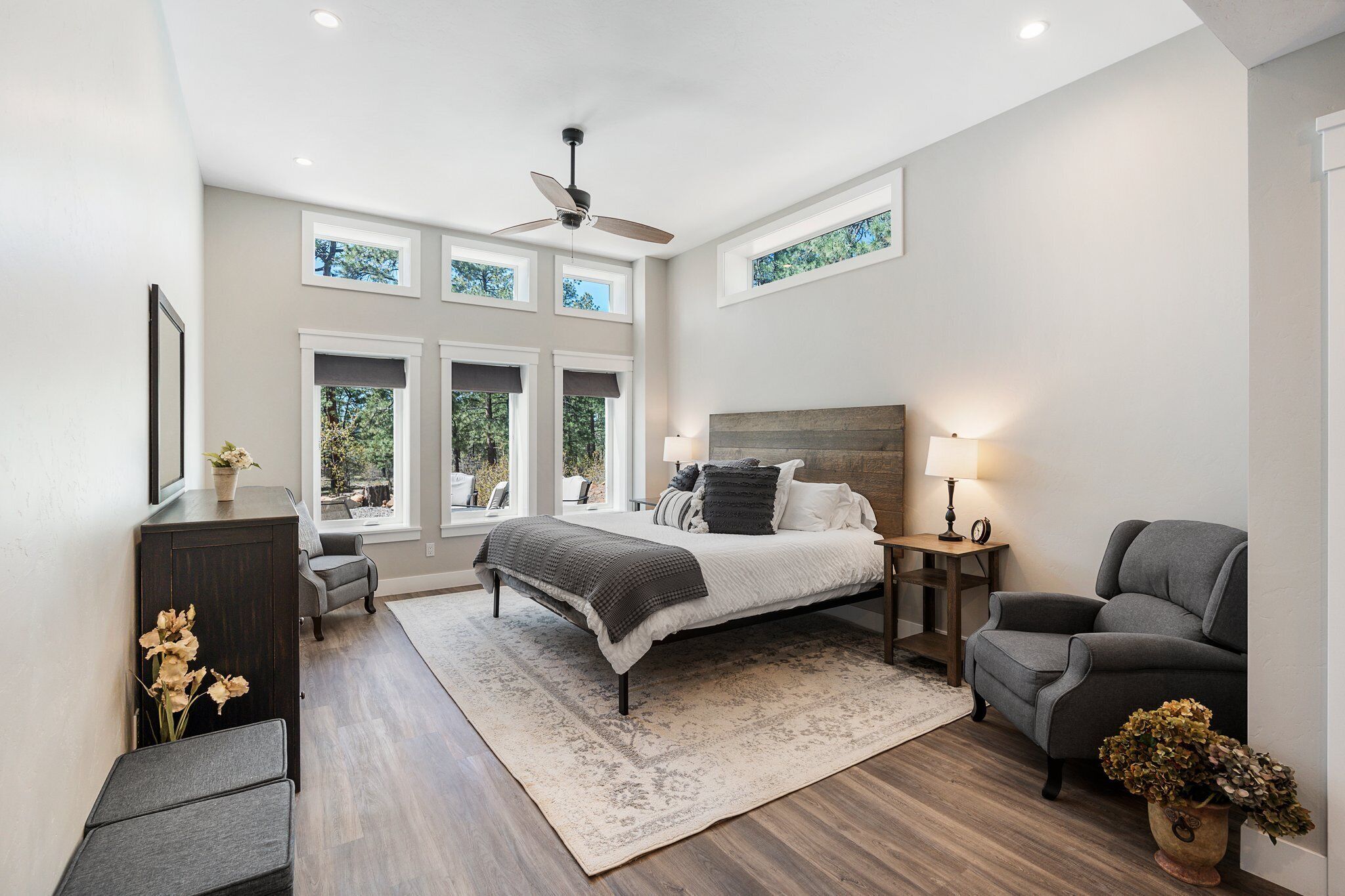 A bedroom with a bed, a desk, a chair, a floor lamp, and a window with a view of trees.