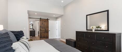 A bedroom with a large bed, dark wooden dresser, and a mirror above it.