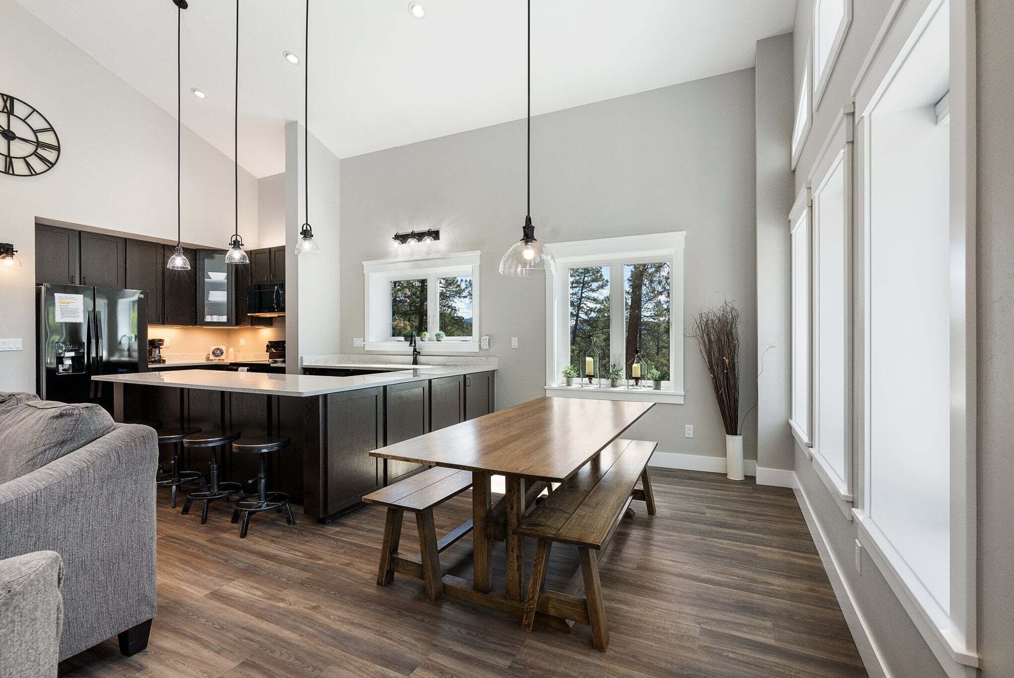 A modern kitchen with a central island, pendant lighting, and a large window with a view of trees.