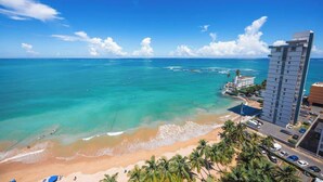 Un hotel frente a la playa con vista al océano, una playa de arena y palmeras.