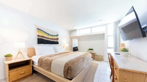 Una habitación de hotel moderna con cama, mesitas de noche, un escritorio y una televisión.