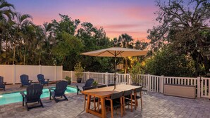 An outdoor patio with a pool, wooden table, chairs, and an umbrella. - Canal-Front Oasis in Terra Ceia: Pool, Patio, Dock (Terra Ceia)