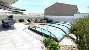 Una piscina con cerramiento de vidrio, mobiliario exterior y zona de patio.