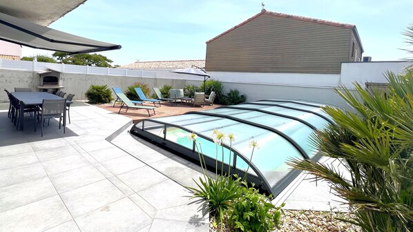 A swimming pool with a glass enclosure, outdoor seating, and a patio area.