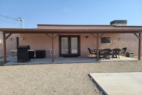 A covered patio area with a grill, outdoor seating, and a building with a sliding glass door.