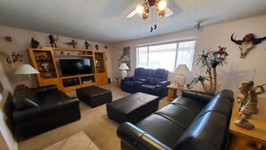 Una sala de estar con un televisor grande, sofás de cuero negro, un mueble de entretenimiento de madera y elementos decorativos en las paredes.