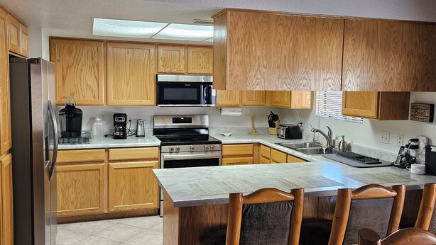Una cocina con armarios de madera, un refrigerador de acero inoxidable, un microondas, un horno y un comedor con mesa y sillas.