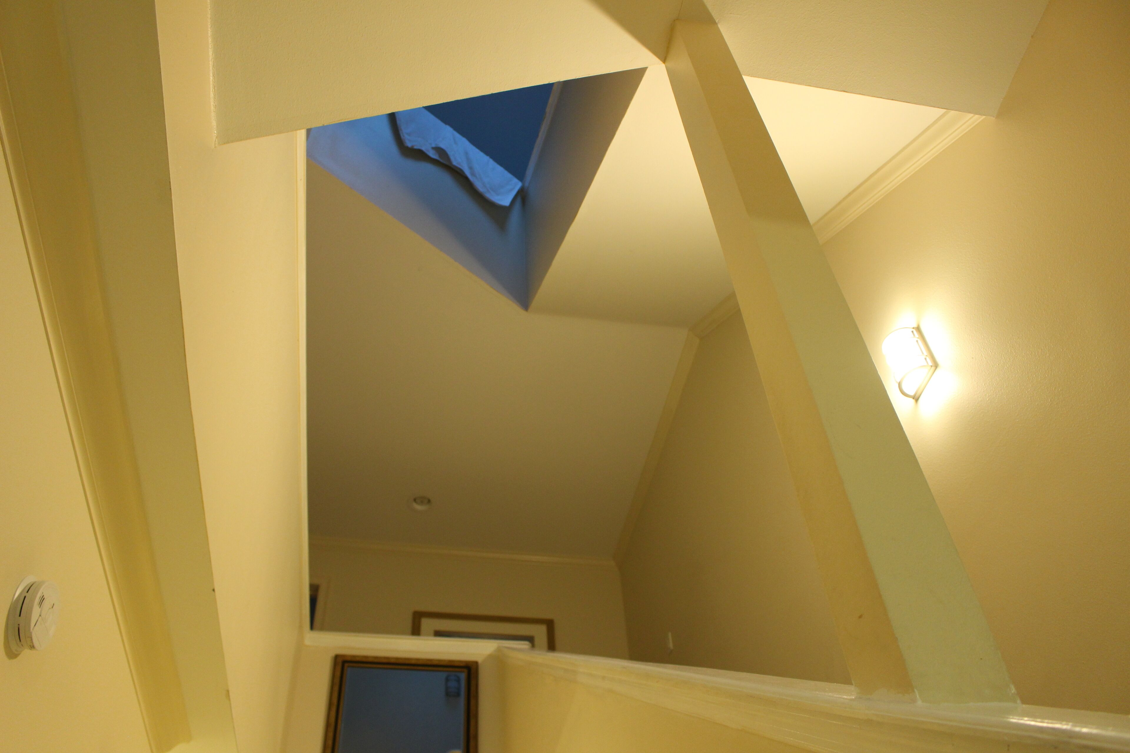 Un escalier avec une lucarne menant à une pièce où se trouve un luminaire fixé au mur.