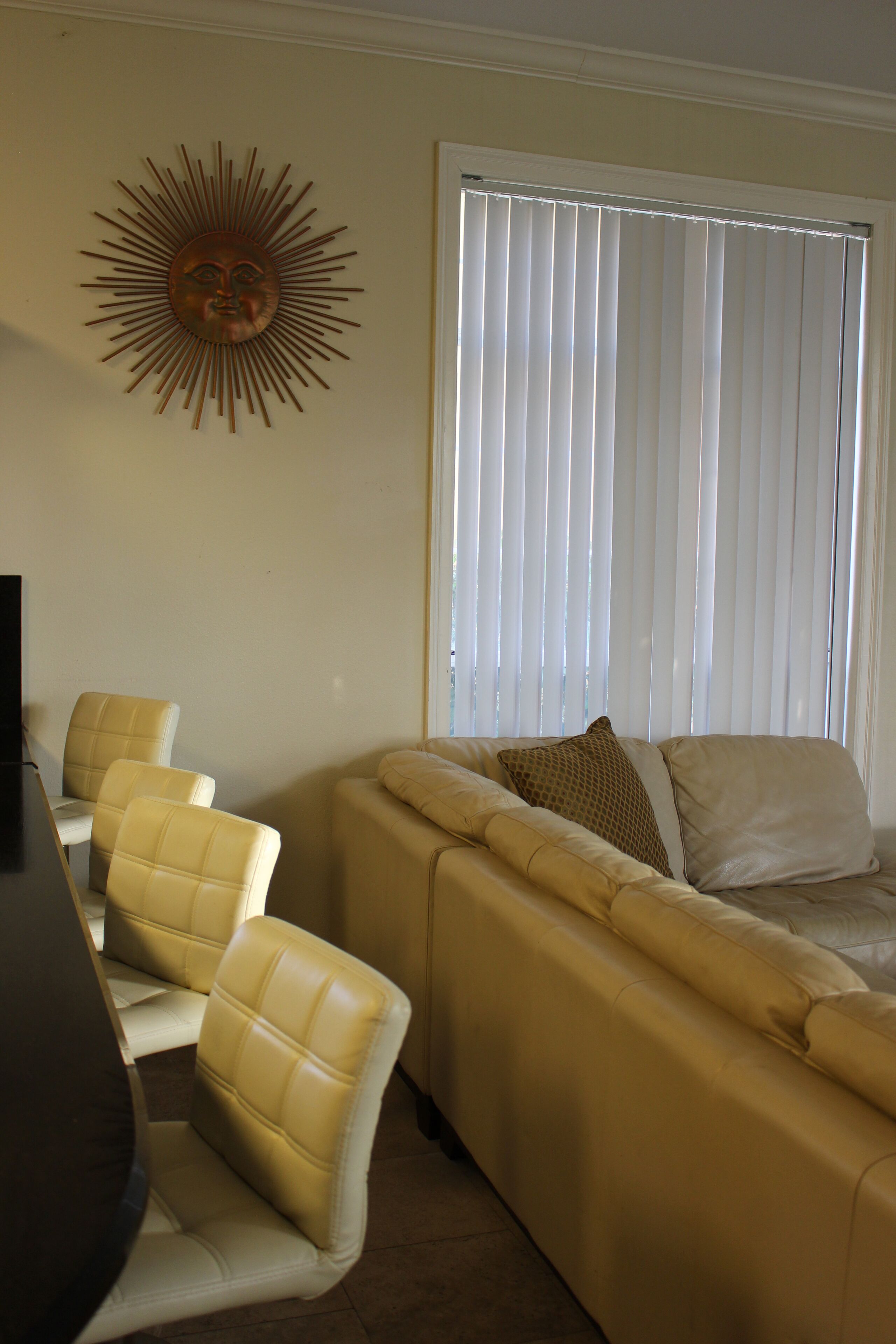 A living room with a beige sofa, two matching armchairs, a coffee table, and a wall-mounted sun decoration.