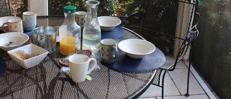 A covered patio with a table set for breakfast, including plates, cups, and a pitcher of orange juice.