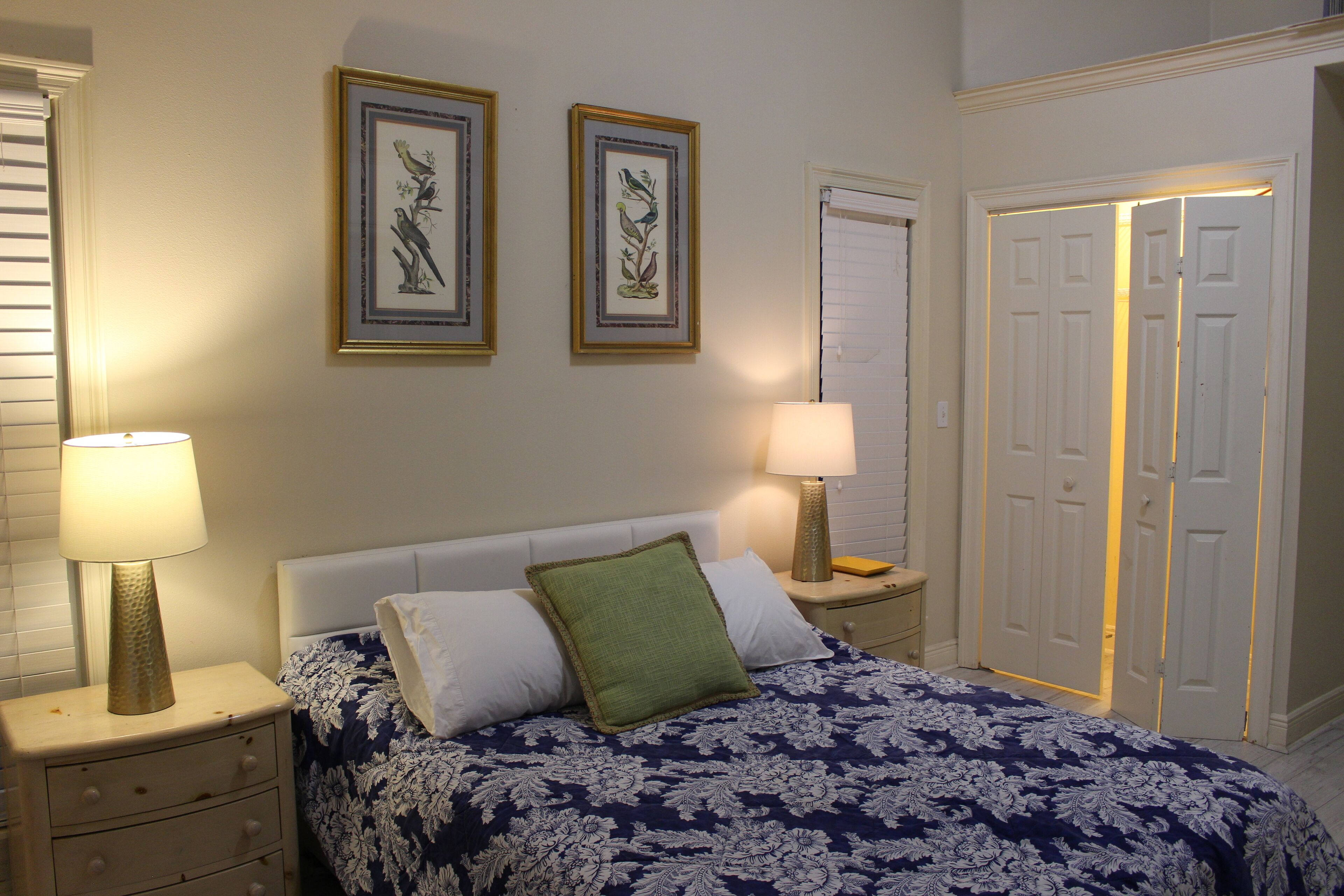 A bedroom with a bed, two bedside lamps, a nightstand, a dresser, and two framed pictures on the wall.
