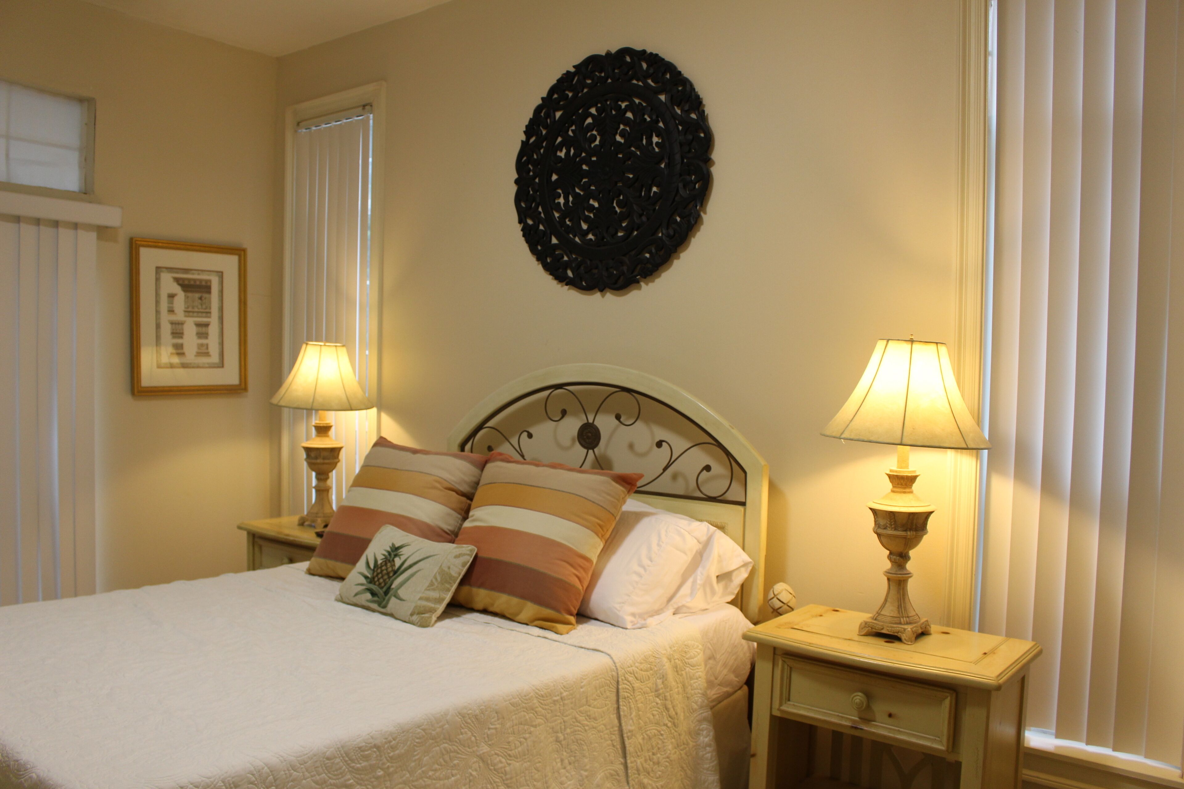 A neatly made bed with striped pillows, two bedside lamps, a decorative wall hanging, and a framed picture on the wall.