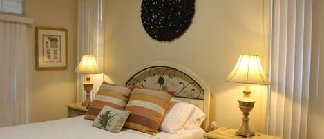 A neatly made bed with striped pillows, two bedside lamps, a decorative wall hanging, and a framed picture on the wall.