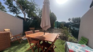 A patio with a wooden table and chairs, an umbrella, and a small table with a floral tablecloth.