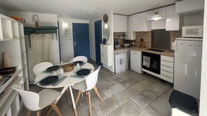 A compact kitchen with white cabinets, a microwave, a refrigerator, and a dining area with white chairs and a table set for four.