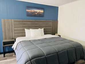 A neatly made bed with a grey quilt, a wooden headboard, and a cityscape painting on the wall. - Crown Inn (Linden)