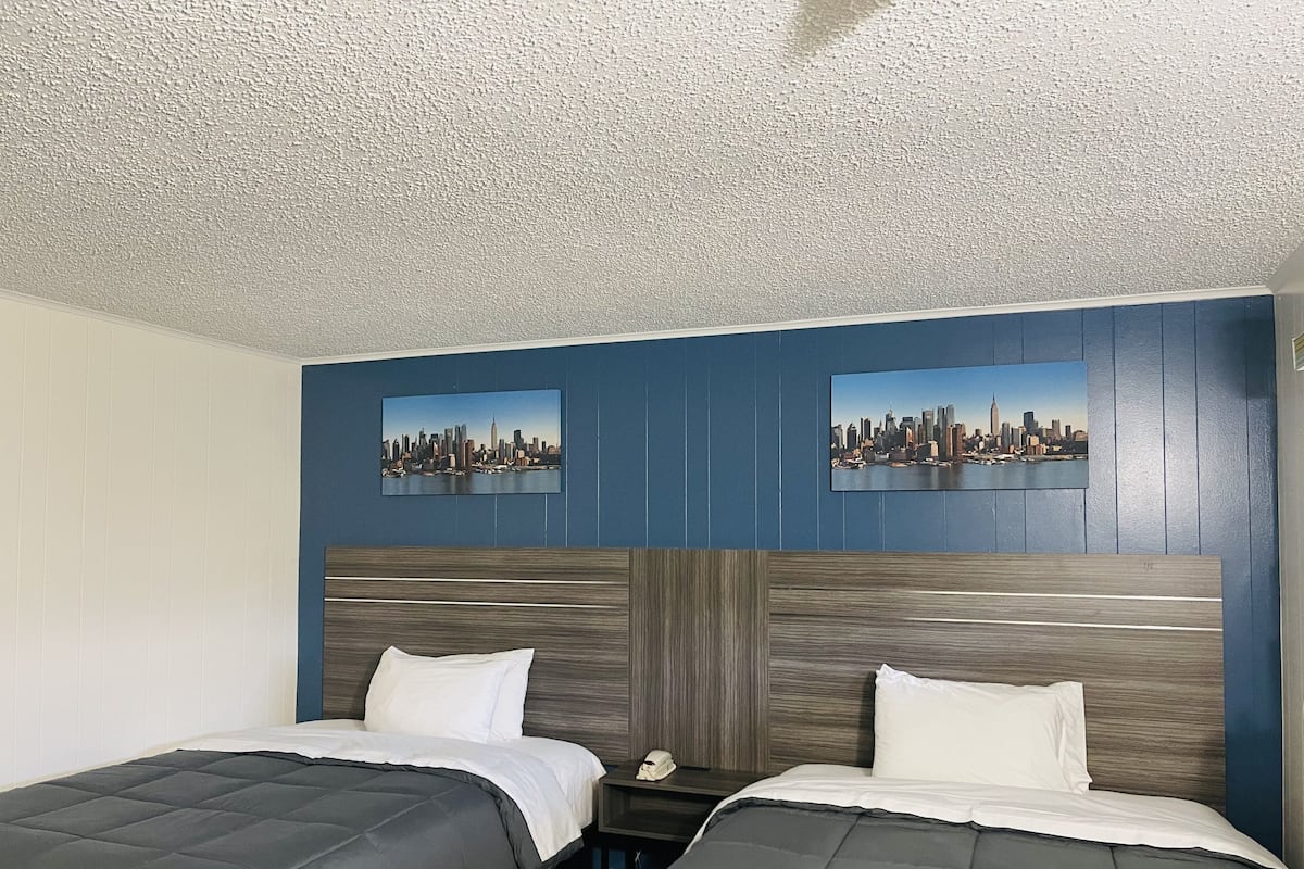 Ett hotellrum med två sängar, en väggdekoration med ett stadsmotiv och en sänggavel i trä.