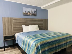 A hotel room with a bed, a nightstand, a headboard, and a cityscape picture on the wall.