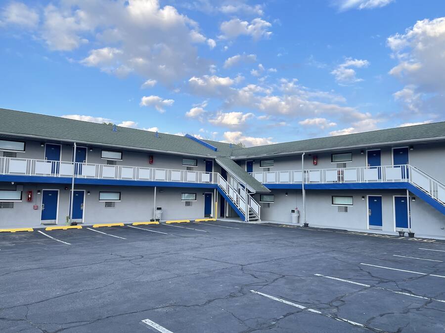 Ein zweistöckiges Motel mit Parkplatz, Außenfassade in Blau und Weiß und einer Treppe, die die Etagen verbindet.