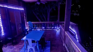 Een terras buiten met een tafel, stoelen, een blauw geruit kleed en een balustrade.