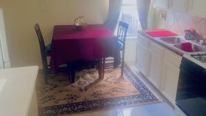 Een kleine keuken met een eettafel, stoelen, een vloerkleed en een spoelbak.