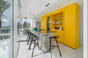 A modern kitchen with a yellow accent wall, a large island with bar stools, and a view of the outdoors.