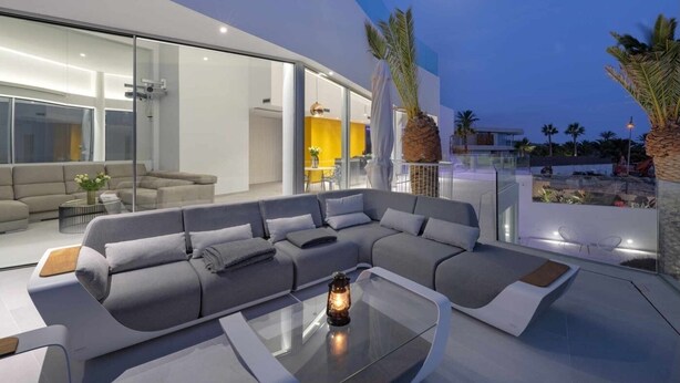 Ein modernes Wohnzimmer mit einem großen Ecksofa, einem Glastisch und Blick ins Freie.