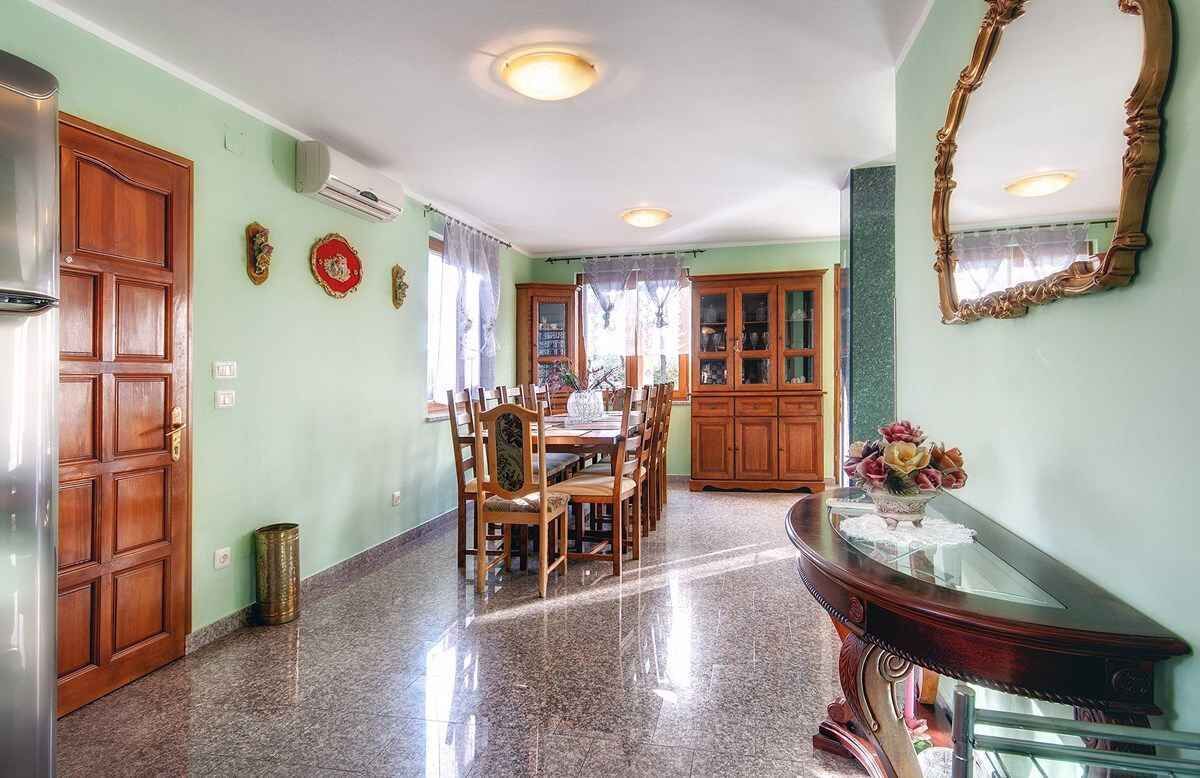 A dining area with a wooden table and chairs, a glass-top console table with a vase, and a large mirror on the wall.