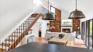 Un vaste espace de vie agrémenté d’un escalier en bois, d’une cheminée et d’une grande table à manger.