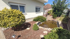 Un jardín residencial con un estanque, varios arbustos y un pequeño sendero de piedra.