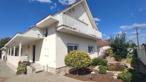 Una casa de dos pisos con fachada blanca, un balcón en el nivel superior y un pequeño jardín con un estanque.