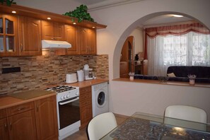 Kitchen area with gas stove, washing machine, and coffee maker, adjacent to a dining space with a glass table and two chairs.