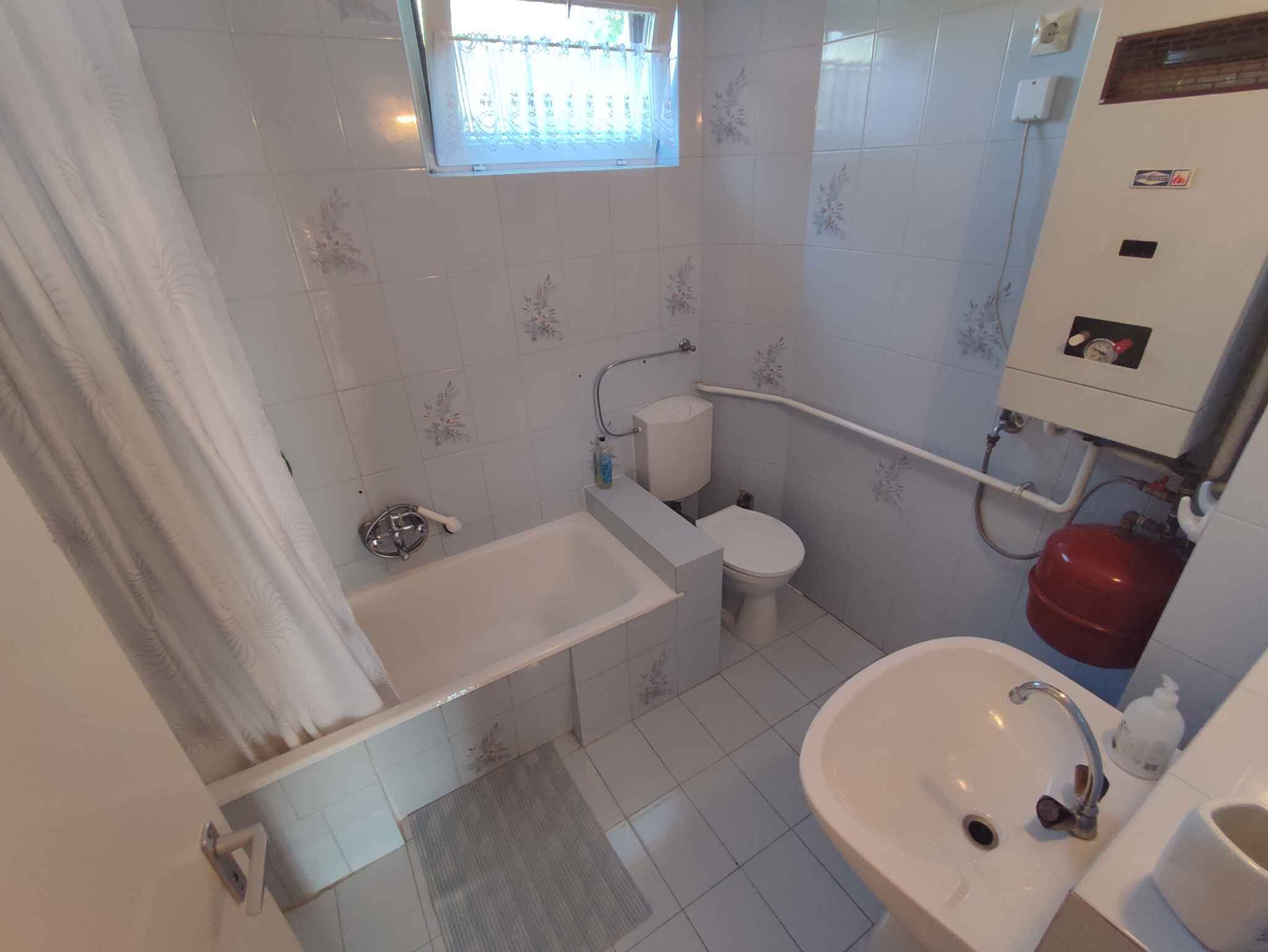Ein Badezimmer mit Badewanne, Toilette, Waschbecken und einem Fenster mit Vorhang.