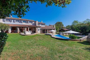 A large house with a swimming pool, a covered patio, and a well-maintained lawn.