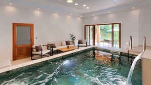A modern indoor pool area with a seating area, a wooden door, and a view of the outdoors. - Villa with swimming pool, sauna and indoor pool (Nedešćina)